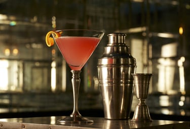 Pink cocktail in a glass next to cocktail shaker and measure on a table in Art Deco mirrored bar