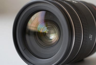 Close-up of a professional camera lens showing complex glass elements and multi-layered coatings, charcoal gray finish, sharp focus with soft bokeh, studio lighting in a North American setting.