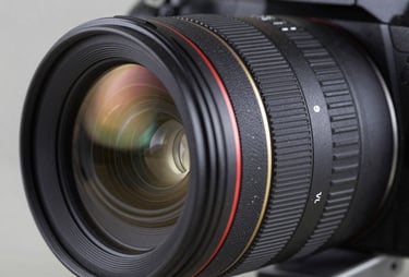 A close-up photograph of a professional camera lens with reflections of a modern studio, charcoal black and slate blue tones, professional lighting, sharp focus.