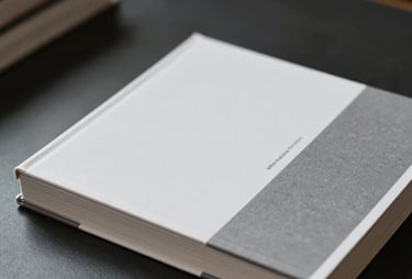 A stack of minimalist design books with white and gray covers on a dark desk. Soft shadows, International / General.
