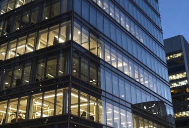 A professional photograph of a modern glass office building at night with lights reflecting on its sleek surface. North American / Global Financial Market.