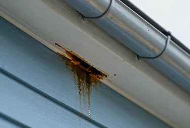 Close-up portrait shot of a sagging gutter pulling away from a fascia board, with visible water stains and rot, under bright daylight. Sharp focus on the damaged area, highlighting the structural problem.