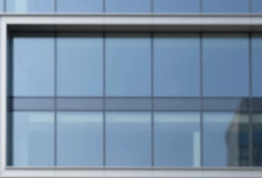 A minimalist wide shot of a contemporary building facade with large glass panels reflecting a clear blue sky, in a professional architectural style.