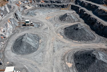 A wide aerial photograph of an industrial quarry facility at midday, with clear pathways and organized material stockpiles in shades of gray.
