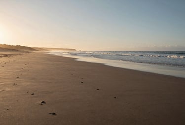 Wide shot of a peaceful Portuguese coastline at sunrise, soft sand beach, cinematic lighting, calm and authentic atmosphere.