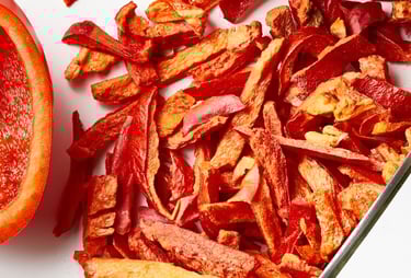 A whole red pepper next to a sliced piece of Thrive freeze-dried red pepper