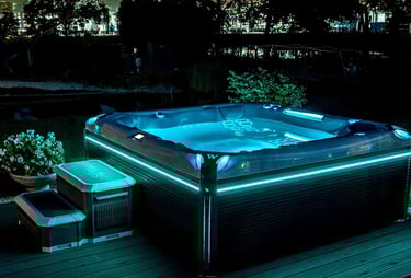 Luxury outdoor hot tub with glowing blue LED lighting on a wooden deck at night.