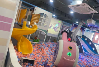 Indoor children's playground featuring a yellow spiral slide, large ball pit, and interactive play equipment.