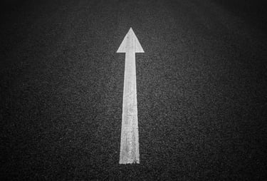 a white arrow pointing up to the left side of a road