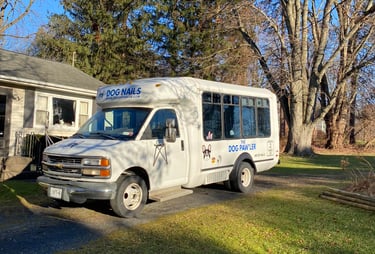 A white The Dog Pawler mobile dog grooming van parked on a residential driveway on a sunny day.