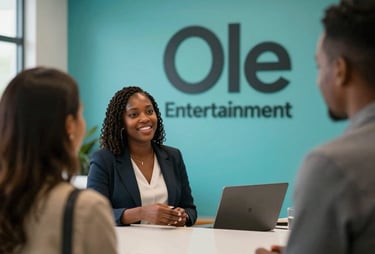 A brightly lit modern lobby of a media company. An African / Pan-African woman is greeting guests, with a large logo of 'Ole Entertainment' on a teal wall in the background.