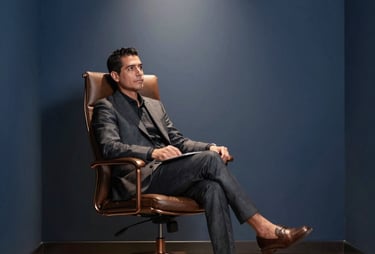 A minimalist, dark blue office corner with a high-end chair and a soft spotlight. Sophisticated Latin American / Hispanic executive feel, warm bronze accents.