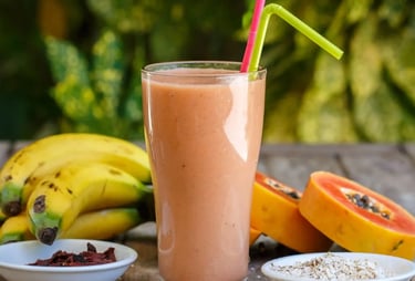whey protein na mesa com frutas ao fundo (banana, mamão m ) + um copo de shake pronto ao lado