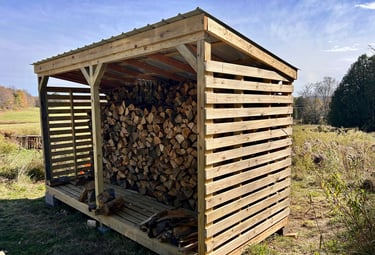 a wooden storage shed with logs stacked on top of it