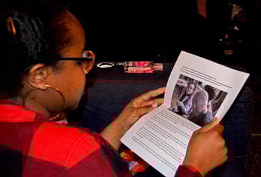 a Black woman reading from paper while sitting on a couch
