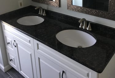 Double vanity with white shaker cabinets, dark countertop, and bronze mosaic mirror frames
