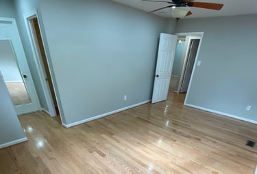 Wide bedroom view showing refinished hardwood flooring and white trim