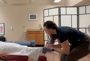 Chiropractor adjusting patient's foot while patient lays on back on chiropractic table.
