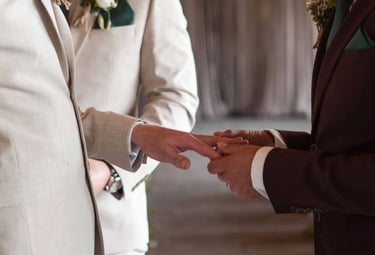 man slides ring onto his husbands hand on their wedding day