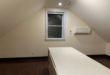 Attic room with sloped ceilings, hardwood floor, window, mini-split AC, and storage cabinet
