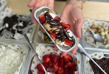 a person holding dessert in front of a table filled with toppings