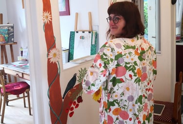 Photo de l'artiste-peintre Marie Hardy devant une fresque d'arbre réalisée dans le salon d'un particulier en Normandie