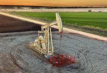 An oil pump jack operates in a rural field during a golden sunset, representing energy production.