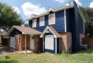 Two-story home with navy blue siding, white trim, and red brick exterior under a sunny sky.