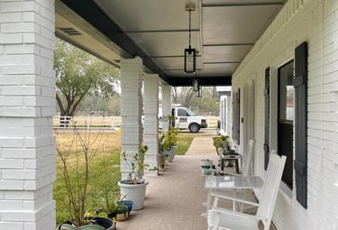 White rocking chairs on a covered ranch-style porch with white brick pillars and blue accents.