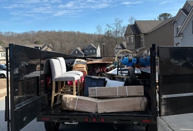 A junk removal trailer filled with furniture, boxes, and debris parked in a residential neighborhood.