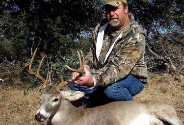 A successful hunter in camouflage posing with a harvested whitetail buck on a Mason County Texas ranch.