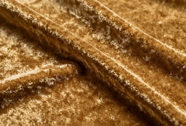 A close-up photograph of rich, deep classic gold velvet fabric. The texture is plush and thick, with elegant shadows created by gentle folds.