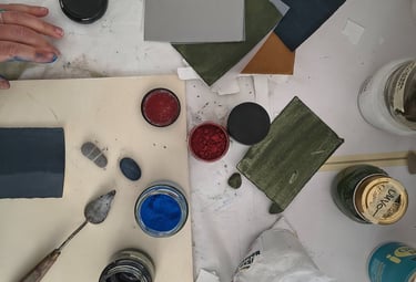 Overhead view of an artist workstation with pigment powders, paint swatches, and a palette knife.