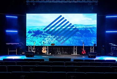 Professional concert stage with a large LED video wall and musical instruments under blue lighting.