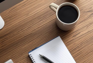 Wooden desk with a computer with a notebook and a pen, and a cup of coffee