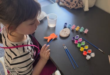 Young girl in a striped shirt painting ceramic Easter eggs and shapes with colorful acrylic paints.