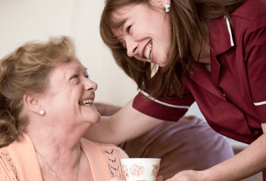 Image of an AMG Nursing & Care Services nurse smiling and proving a cup of tea to a patient in her home