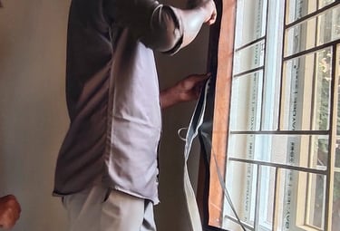 Technician carefully installing a mosquito net on a metal window frame in a Bangalore home.