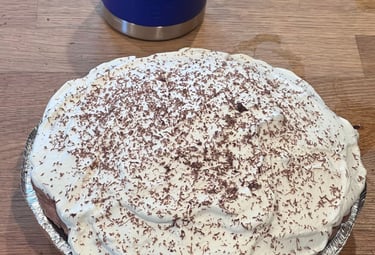 A homemade chocolate silk pie with whipped cream and chocolate shavings next to a blue travel mug.