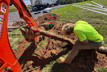 excavator digging up log with man helping