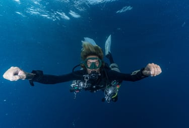 A scuba diver in full gear glides through clear blue ocean water during a deep sea dive.
