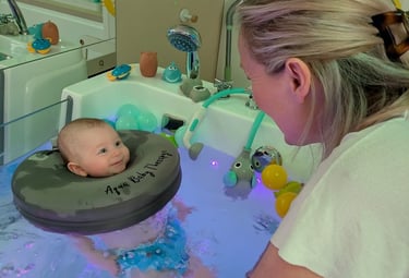 bébé souriant à la praticienne pendant qu'il est dans le bain avec sa bouée de cou