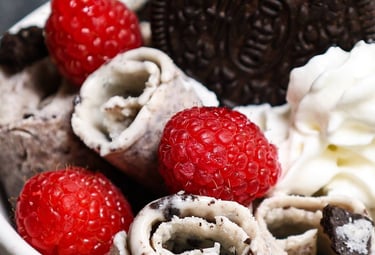 Cookies and cream rolled ice cream topped with fresh raspberries, whipped cream, and an Oreo cookie.