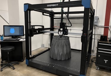 A large-scale Gigabot X2 industrial 3D printer manufacturing a grey geometric structure in a workshop.