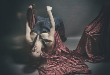 Artistic portrait of a woman in denim overalls posing upside down on red velvet fabric.