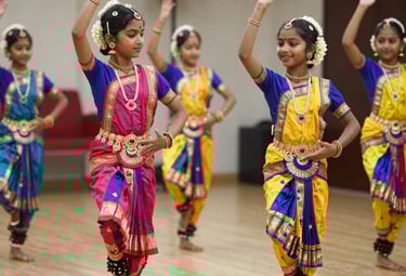 A group of kids joyfully performing a classical dance routine on a bright stage.