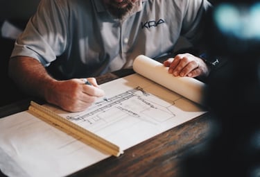 An architect drafting detailed building blueprints and construction plans at a wooden desk.