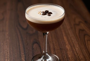 Moody photography of a coffee-based cocktail in a coupe glass, garnished with roasted beans, set against a dark walnut wood background in a sophisticated bar.