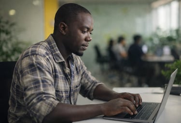 Focused Black businessman working on a laptop at his office desk in a modern workspace.