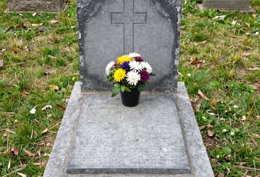 An ornate weathered marble headstone with green moss and dried flowers in an autumn graveyard.
